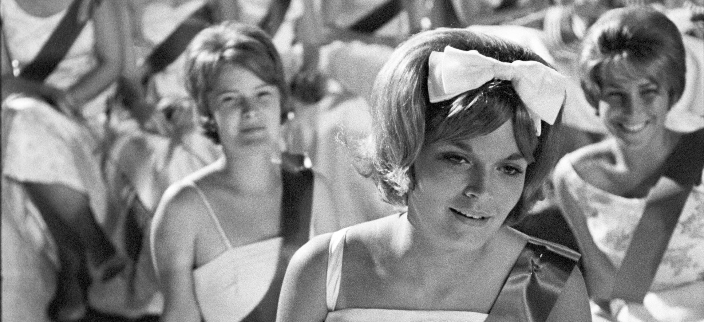 sitzende Frauenmenge mit weißen Ballkleidern und Scherpe und USA Handfähnchen