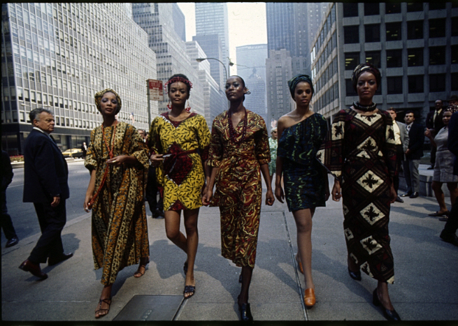 Auf dem Farbfoto sind vier schwarze Frauenmodelle in farbigen Kleidern aus afrikanischen Stoffen vor der Skyline von Manhattan abgebildet
