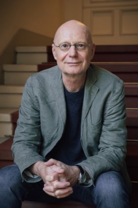 Jens Siegert Ein Mann um die 60 sitzt mit zusammengefalteten Händen auf einer Treppe. Er blickt uns zuversichtlich an .